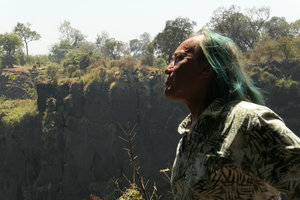 Patrick Blanc looking at a vertical cliff covered by the red flowering Aloe chabaudii receiving continuous water spray, Victoria Falls, Zimbabwe, Sept. 2017