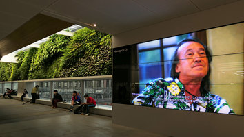 Patrick Blanc on the screen, just beside his vertical garden at the Shinkansen station, Yamaguchi, Japan, April 2017
